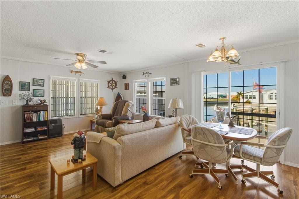 Living room featuring a water view, a ceiling fan, wood finished floors, a textured ceiling, and a chandelier