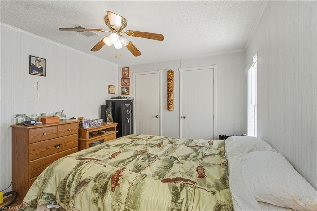 Bedroom featuring ornamental molding, two closets, a ceiling fan, and a textured ceiling