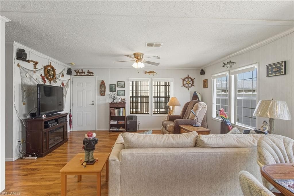 Living room featuring wood finished floors, ceiling fan, a textured ceiling, and crown molding