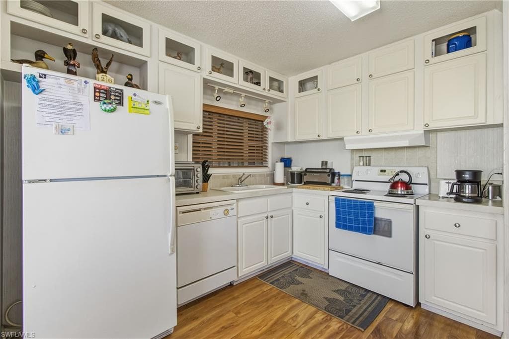 Kitchen featuring white appliances, glass insert cabinets, a textured ceiling, white cabinets, and light countertops