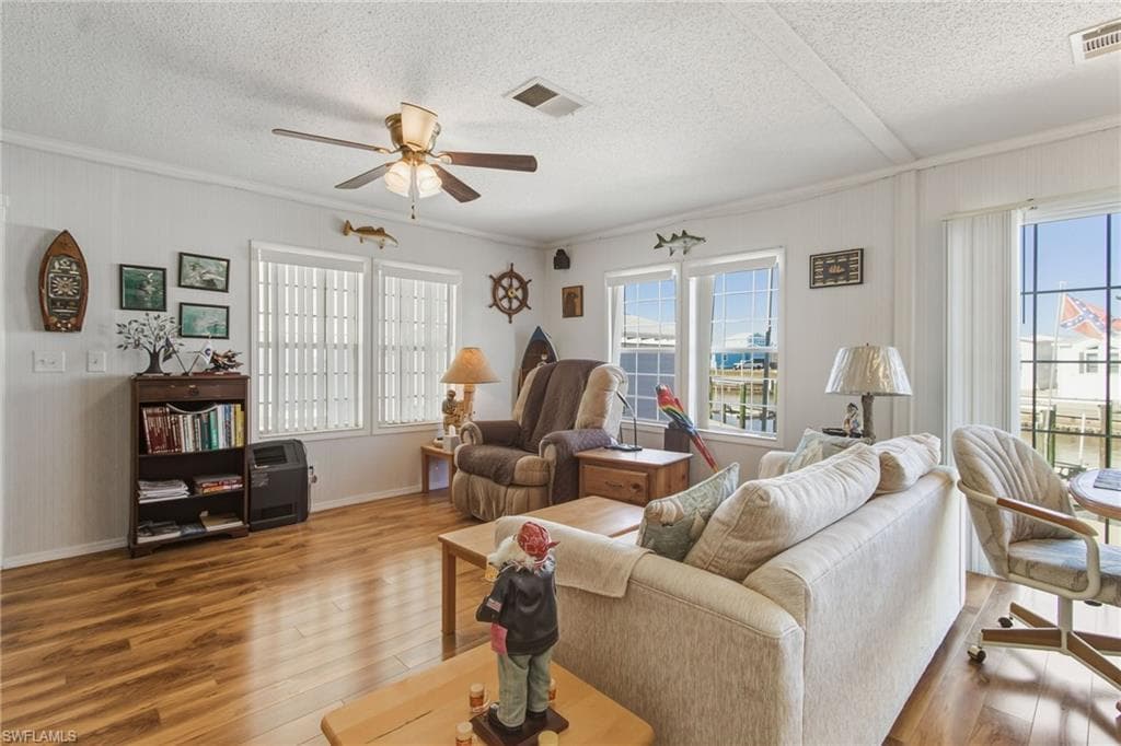 Living room with light wood-style floors, plenty of natural light, a ceiling fan, a textured ceiling, and ornamental molding