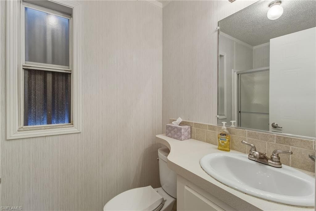 Full bath featuring a stall shower, vanity, a textured ceiling, decorative backsplash, and crown molding