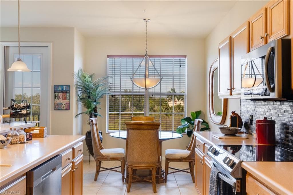 Kitchen featuring stainless steel appliances, light countertops, light tile patterned floors, and decorative light fixtures