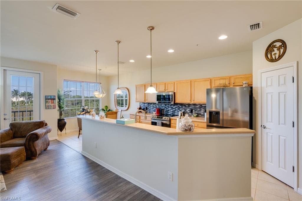Kitchen with light brown cabinets, light countertops, stainless steel appliances, pendant lighting, and backsplash