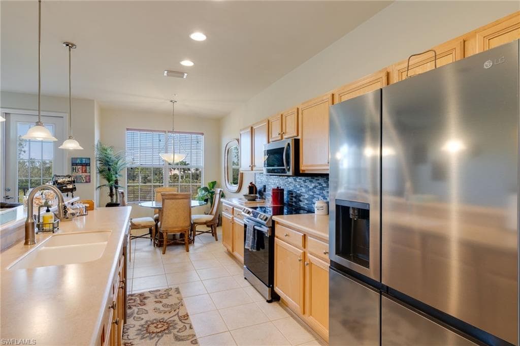 Kitchen with stainless steel appliances, decorative light fixtures, light brown cabinets, recessed lighting, and light countertops