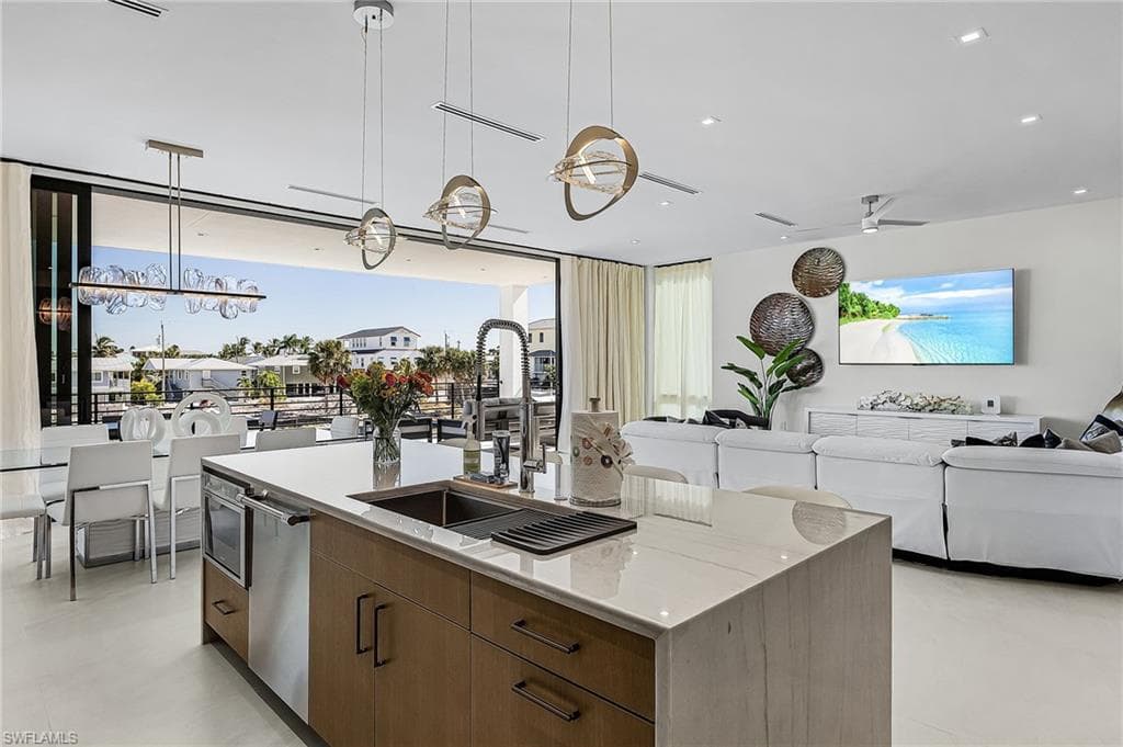 Kitchen featuring brown cabinetry, hanging light fixtures, modern cabinets, open floor plan, and a kitchen island with sink - Virtually Edited Image