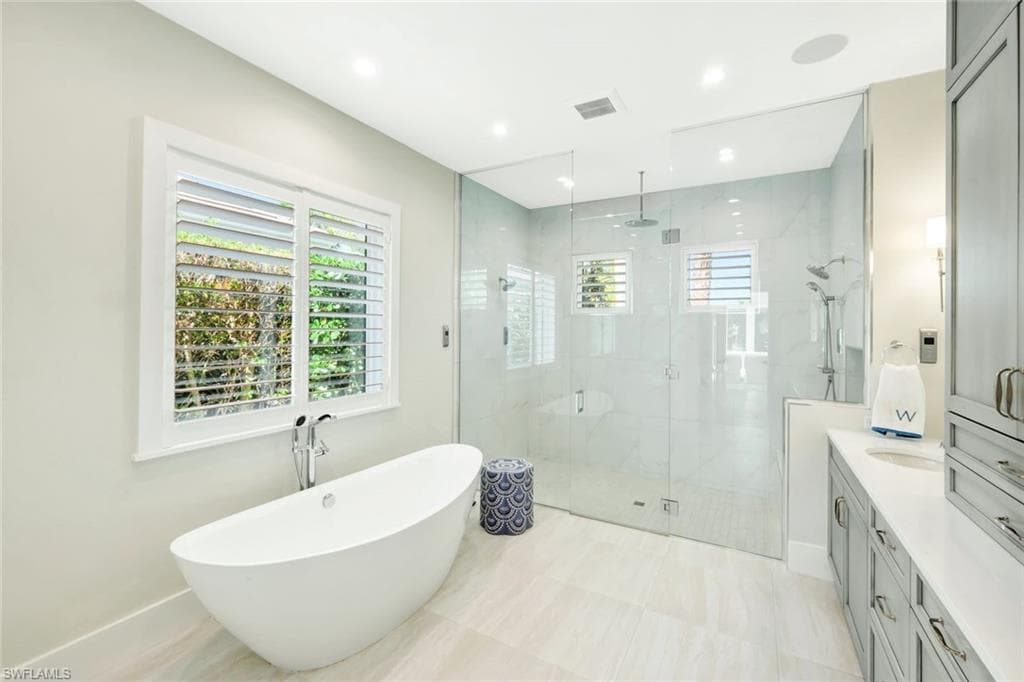Bathroom featuring vanity, a freestanding tub, a shower stall, recessed lighting, and light tile patterned flooring