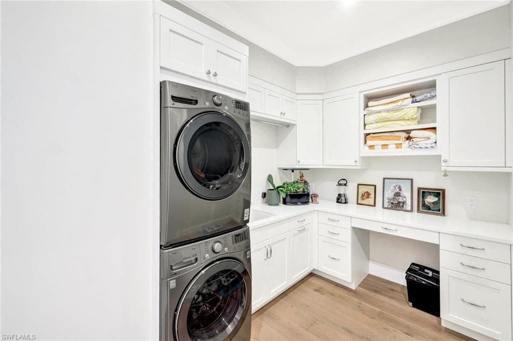 Laundry room featuring cabinet space, light wood finished floors, stacked washer / drying machine, and an office area