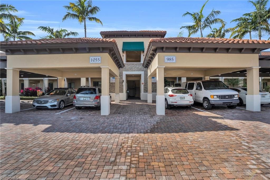 View front of complex with a tiled roof, stucco siding, stone siding, and covered parking