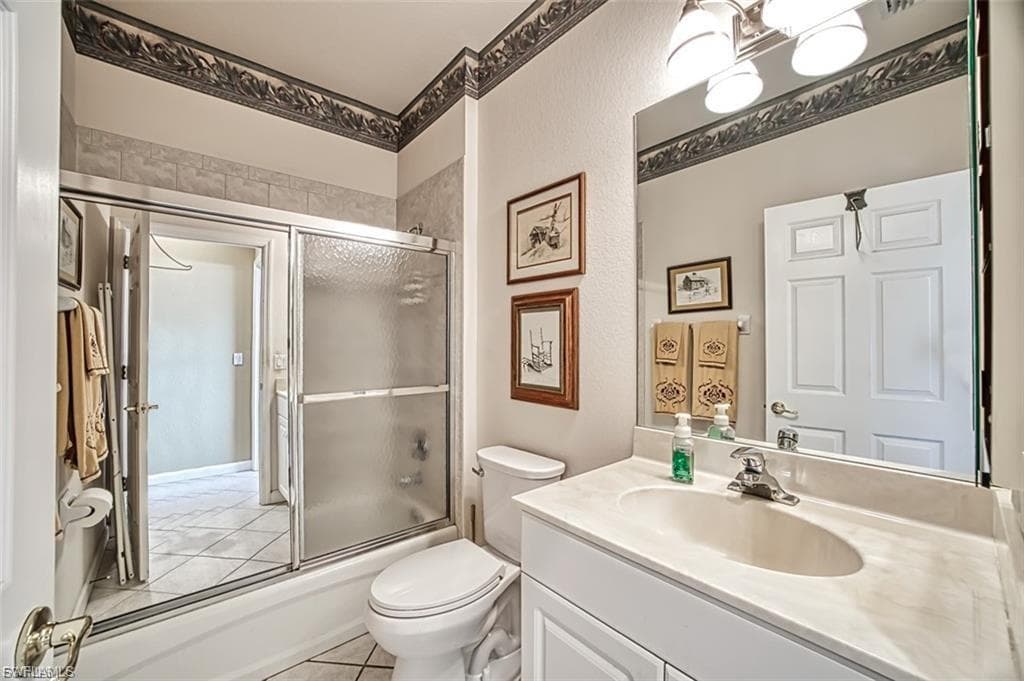 Full bath with bath / shower combo with glass door, vanity, and light tile patterned floors