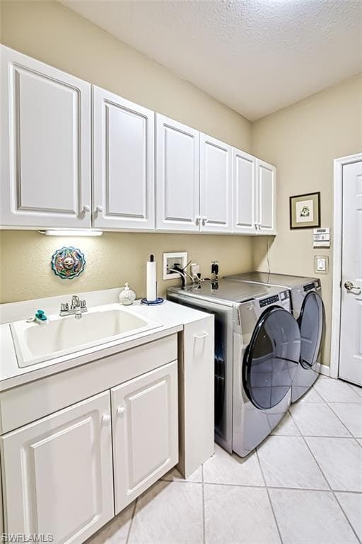 Washroom featuring light tile patterned flooring, a textured ceiling, cabinet space, and washer and dryer