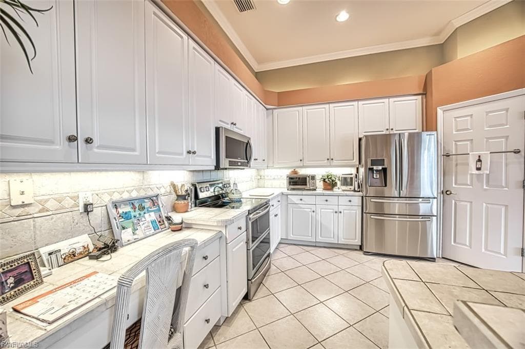 Kitchen featuring appliances with stainless steel finishes, white cabinets, tile countertops, light tile patterned flooring, and crown molding