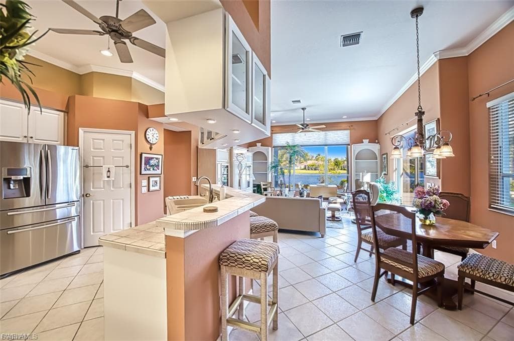 Kitchen featuring a ceiling fan, stainless steel refrigerator with ice dispenser, crown molding, light tile patterned floors, and tile counters