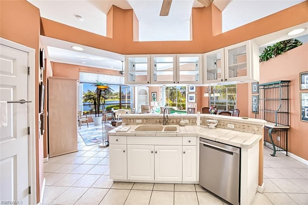 Kitchen with white cabinetry, glass insert cabinets, a ceiling fan, a center island with sink, and stainless steel dishwasher