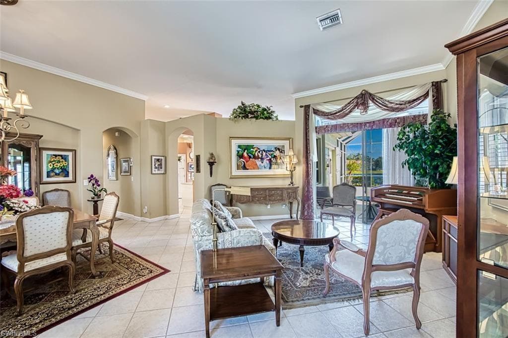 Living area with light tile patterned flooring, crown molding, arched walkways, and a chandelier