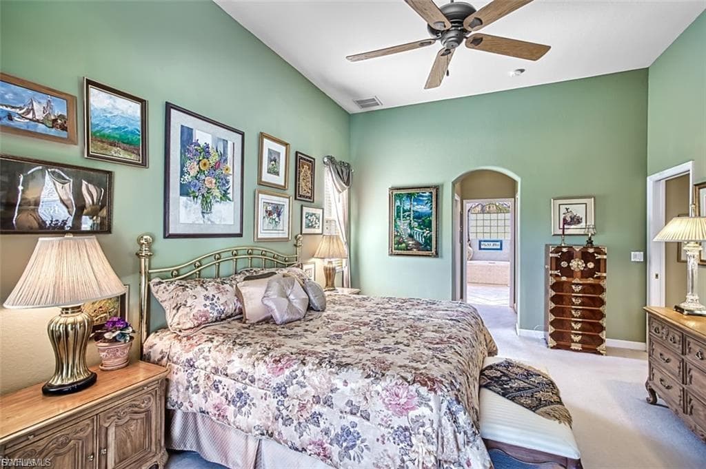 Bedroom with light carpet, ensuite bathroom, arched walkways, and a ceiling fan