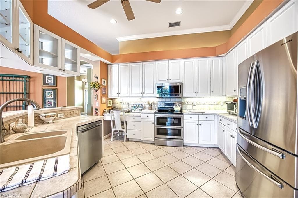 Kitchen with stainless steel appliances, white cabinetry, glass insert cabinets, ornamental molding, and light tile patterned floors