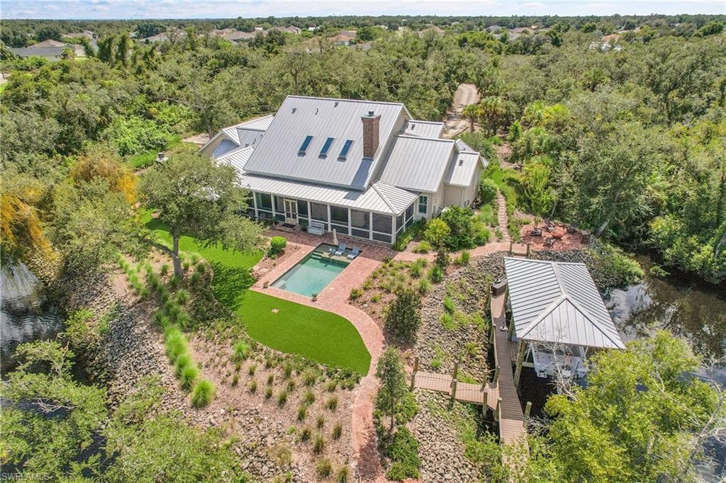 Rear of the home showcasing a resort-style pool, lush synthetic lawn, and private dock, all surrounded by natural landscaping for exceptional privacy