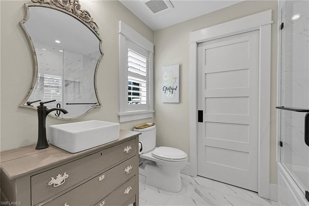 Stylish bathroom featuring a custom vanity with vessel sink, designer mirror, and modern features. Door opens into full walk-in closet