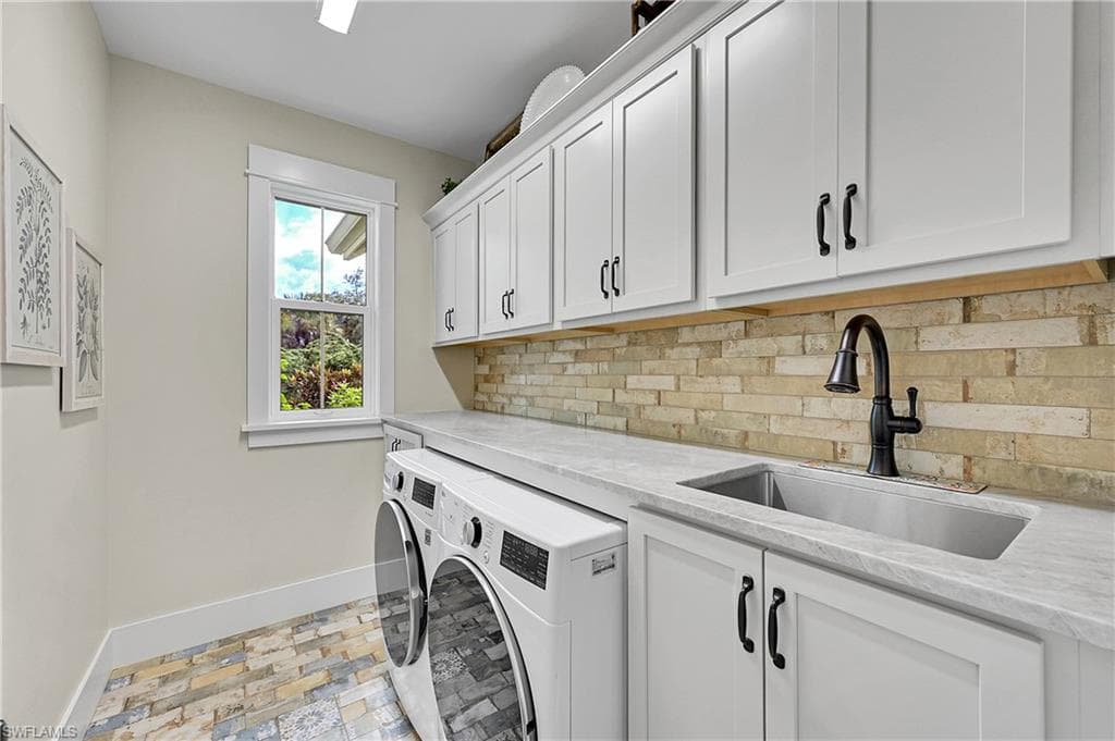 Well-appointed laundry room featuring custom cabinetry, stone countertops, utility sink and full-size washer and dryer