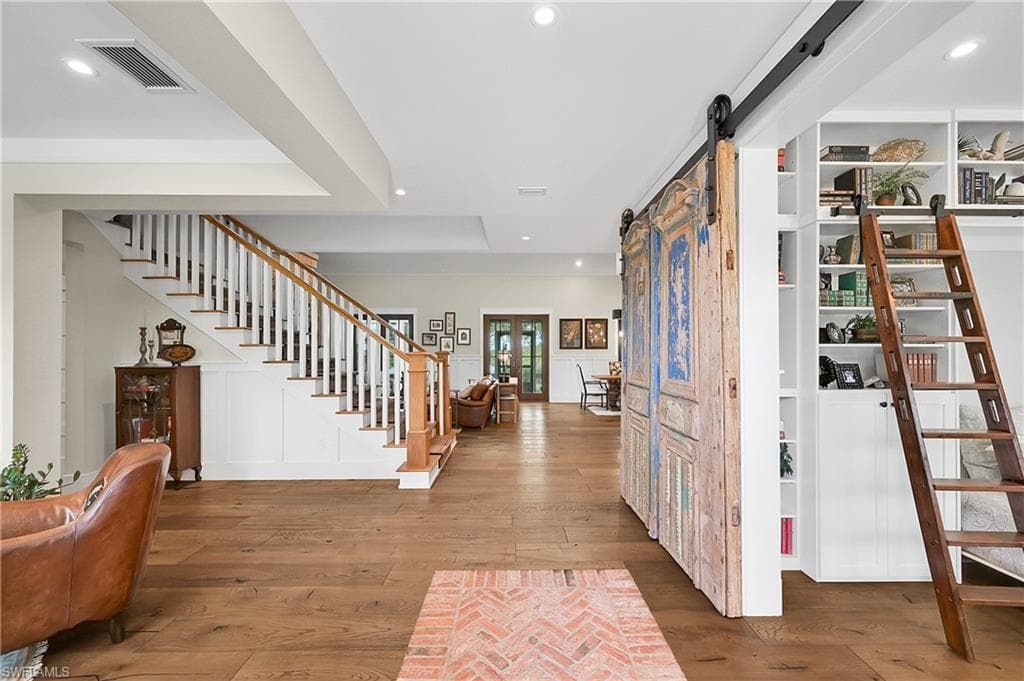 Striking entry foyer featuring custom brick inlay flooring, wide-plank hardwood floors, and an open staircase. The space leads seamlessly into the great room with soaring vaulted ceilings and skylights