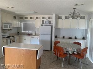 Kitchen with light countertops, a center island, appliances with stainless steel finishes, white cabinets, and vaulted ceiling