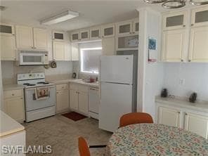 Kitchen featuring white appliances, light countertops, glass insert cabinets, and white cabinets