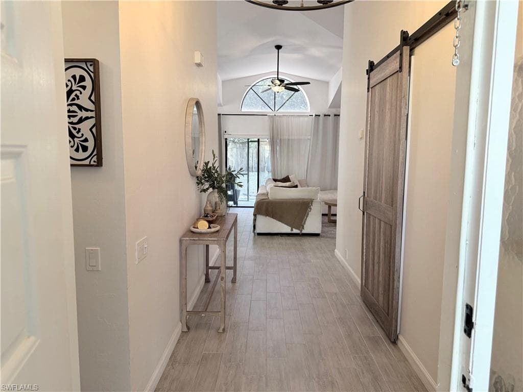 Corridor featuring vaulted ceiling, a barn door, and light wood-style flooring