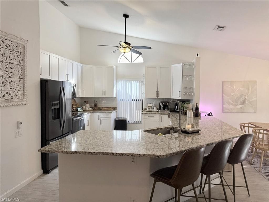 Kitchen with light stone countertops, appliances with stainless steel finishes, a peninsula, a ceiling fan, and high vaulted ceiling