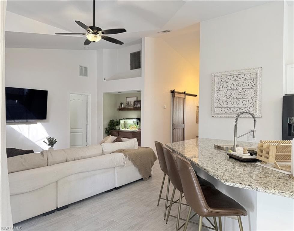 Living area featuring a barn door, ceiling fan, light wood-style floors, and high vaulted ceiling