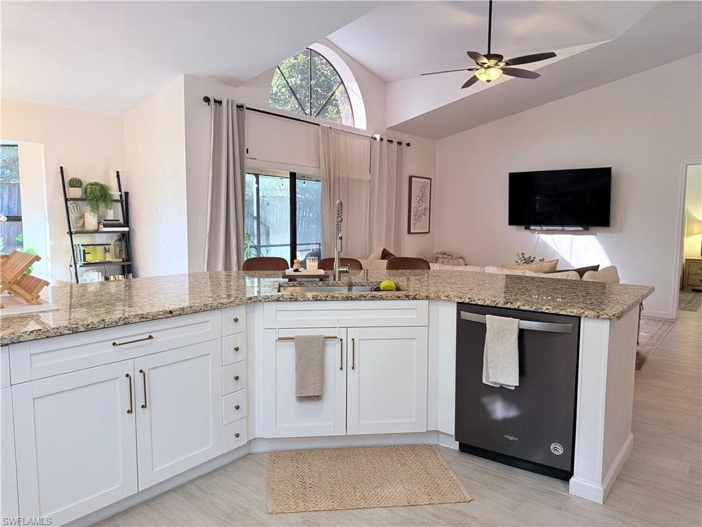 Kitchen featuring open floor plan, white cabinetry, dishwasher, vaulted ceiling, and light stone countertops