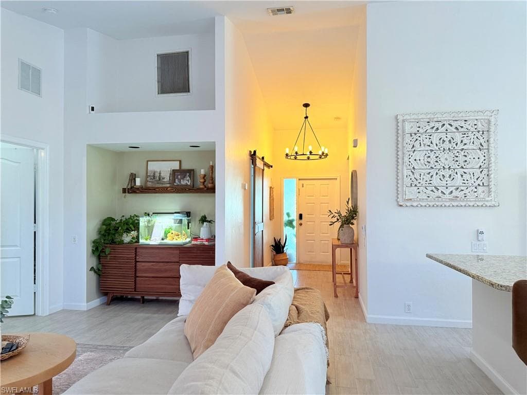 Living room featuring a towering ceiling, a chandelier, a barn door, and light wood-style flooring