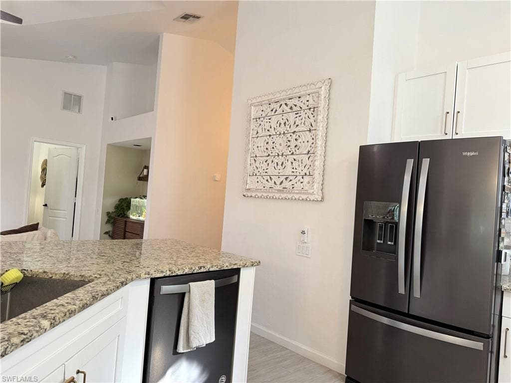 Kitchen featuring white cabinetry, appliances with stainless steel finishes, light stone countertops, light wood-style floors, and lofted ceiling