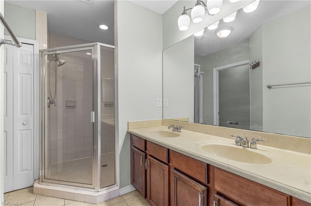 Bathroom with double vanity, a shower stall, and light tile patterned floors