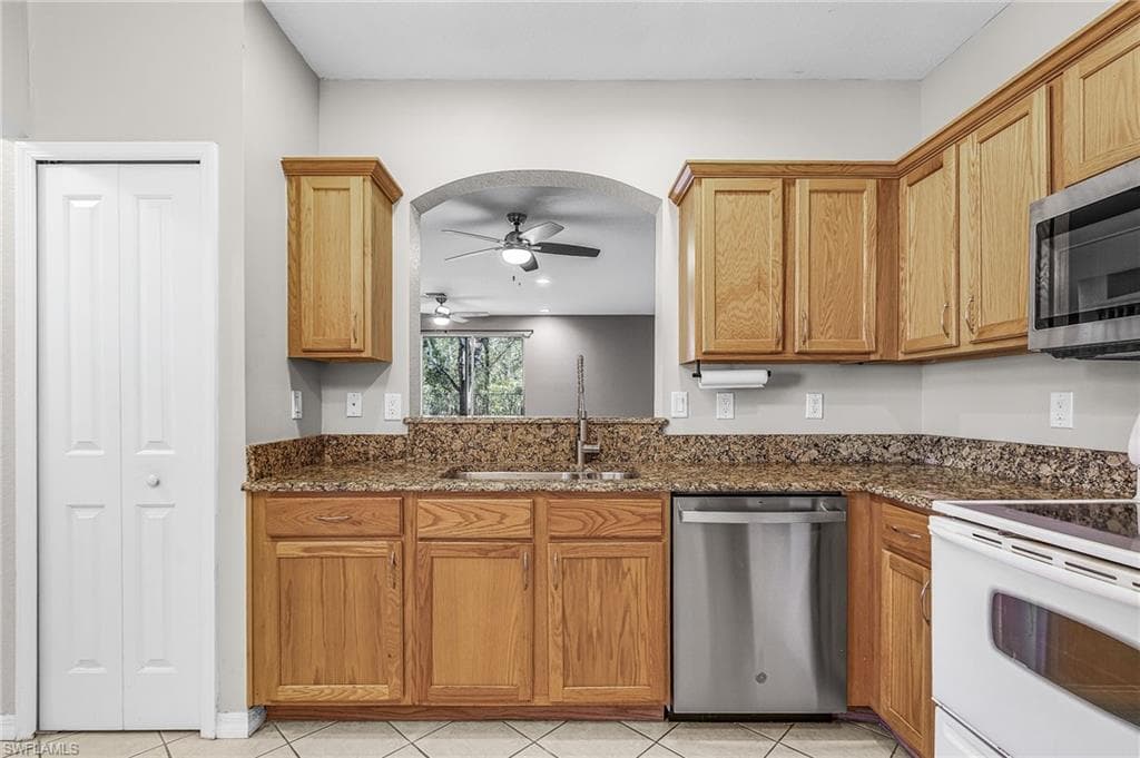 Kitchen with stainless steel appliances, dark stone counters, ceiling fan, light tile patterned floors, and brown cabinets