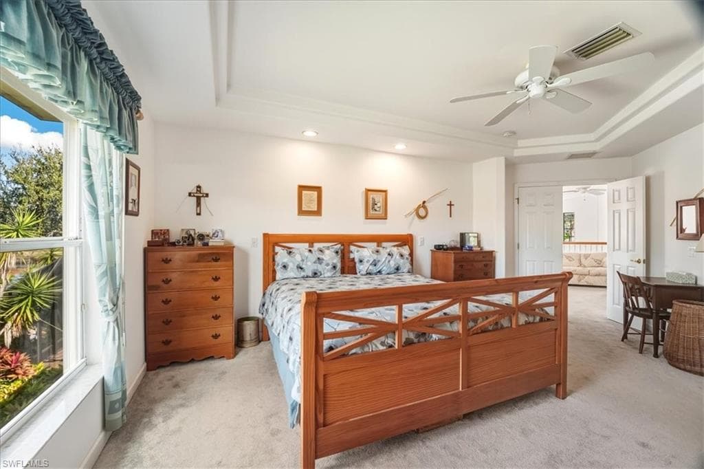 Bedroom with light colored carpet, a raised ceiling, and ceiling fan