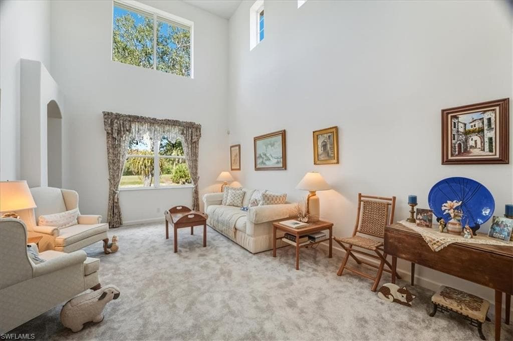 Carpeted living area featuring arched walkways, ornate columns, and a towering ceiling