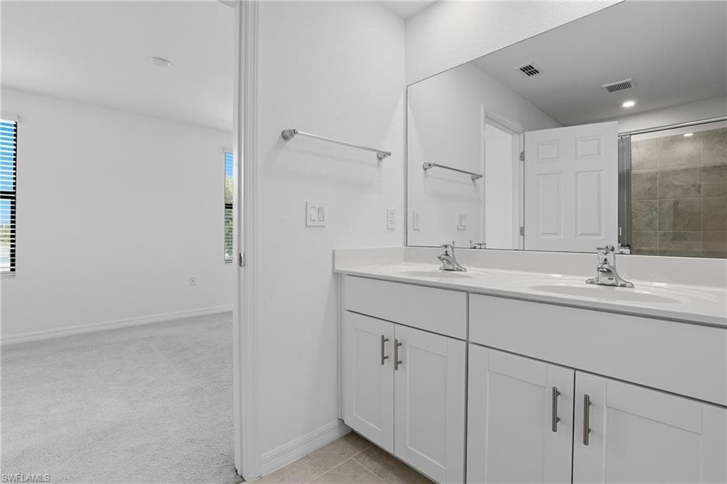Bathroom featuring light colored carpet, double vanity, tiled shower, and recessed lighting