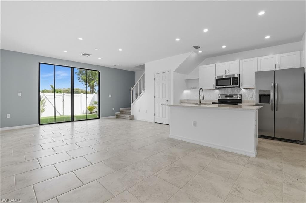 Kitchen with appliances with stainless steel finishes, recessed lighting, an island with sink, white cabinetry, and open floor plan
