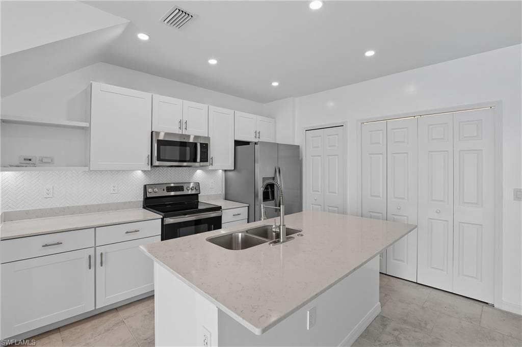 Kitchen with white cabinetry, stainless steel appliances, light stone counters, a kitchen island with sink, and open shelves