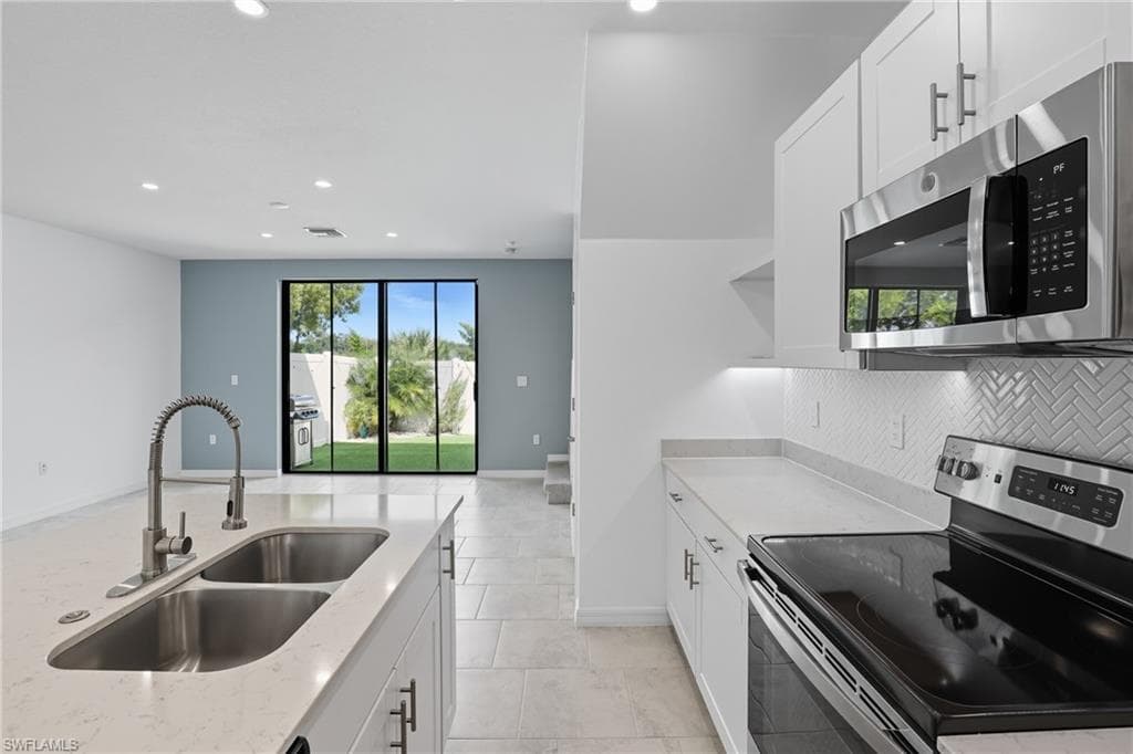 Kitchen with stainless steel appliances, white cabinetry, light stone countertops, healthy amount of natural light, and recessed lighting