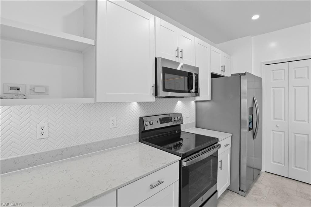 Kitchen with stainless steel appliances, open shelves, white cabinetry, backsplash, and light stone countertops