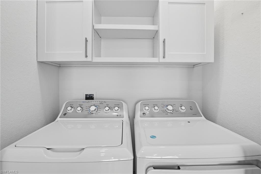 Laundry room with a textured wall, cabinet space, and separate washer and dryer