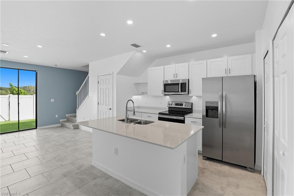 Kitchen with appliances with stainless steel finishes, white cabinetry, light stone countertops, a kitchen island with sink, and backsplash