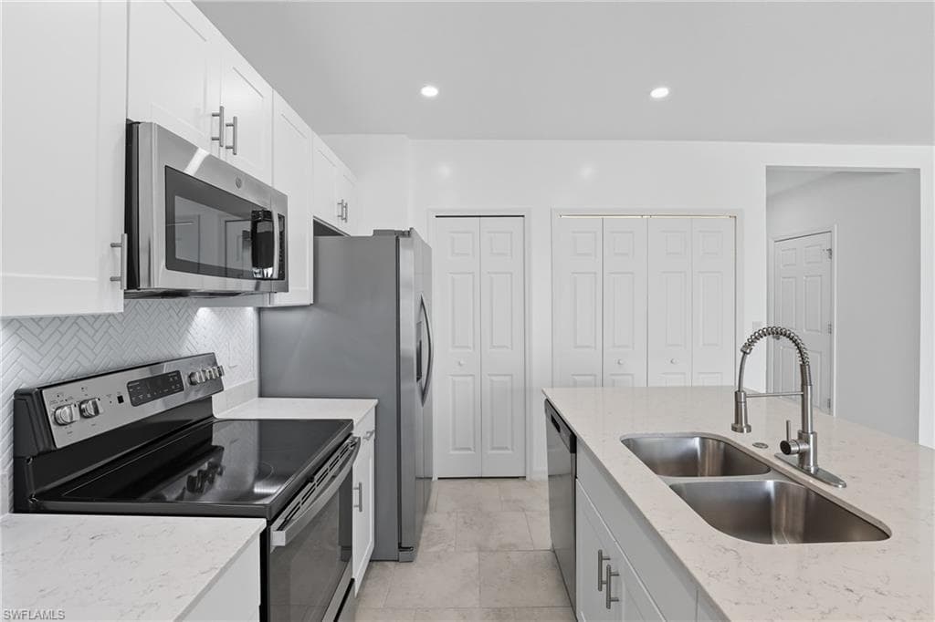 Kitchen with stainless steel appliances, white cabinetry, light stone counters, recessed lighting, and tasteful backsplash
