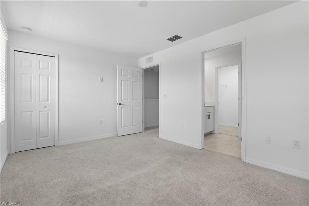Unfurnished bedroom with light carpet, a closet, and ensuite bathroom