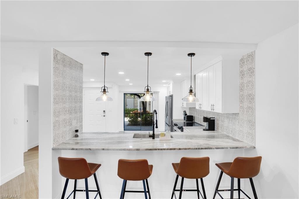Kitchen featuring white cabinetry, a kitchen bar, tasteful backsplash, pendant lighting, and light stone counters