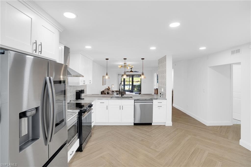 Kitchen featuring stainless steel appliances, white cabinets, wall chimney range hood, pendant lighting, and recessed lighting
