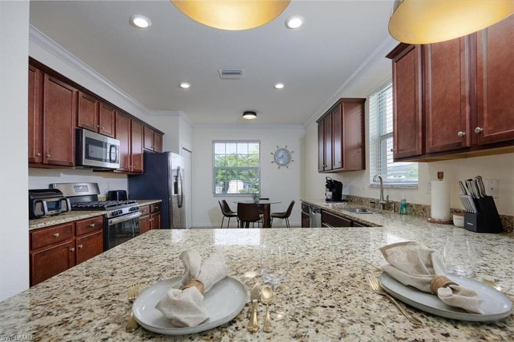 Kitchen featuring ornamental molding, light stone countertops, appliances with stainless steel finishes, and recessed lighting