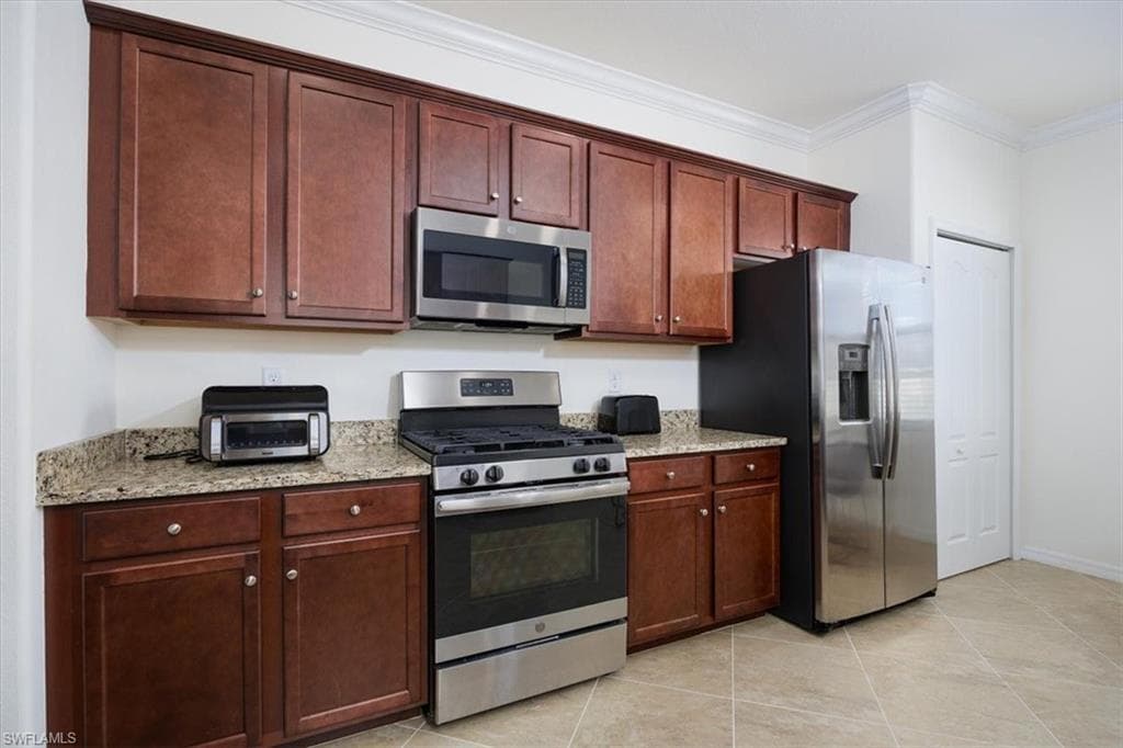 Kitchen with room to add portable island and featuring appliances with stainless steel finishes, light stone counters, ornamental molding, and light tile patterned floors